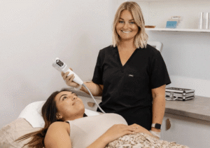 En leende tekniker i svarta arbetskläder utför en kosmetisk behandling på en avslappnad kvinna som ligger ner i en ren och ljus klinik, som visas av en digital marknadsföringsbyrå Stockholm