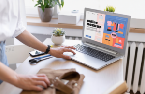 En person står bredvid ett skrivbord med en laptop som visar en mockup av en webbutik. I närheten finns en växt, saxar och kläder. Scenen är ljus och modern.